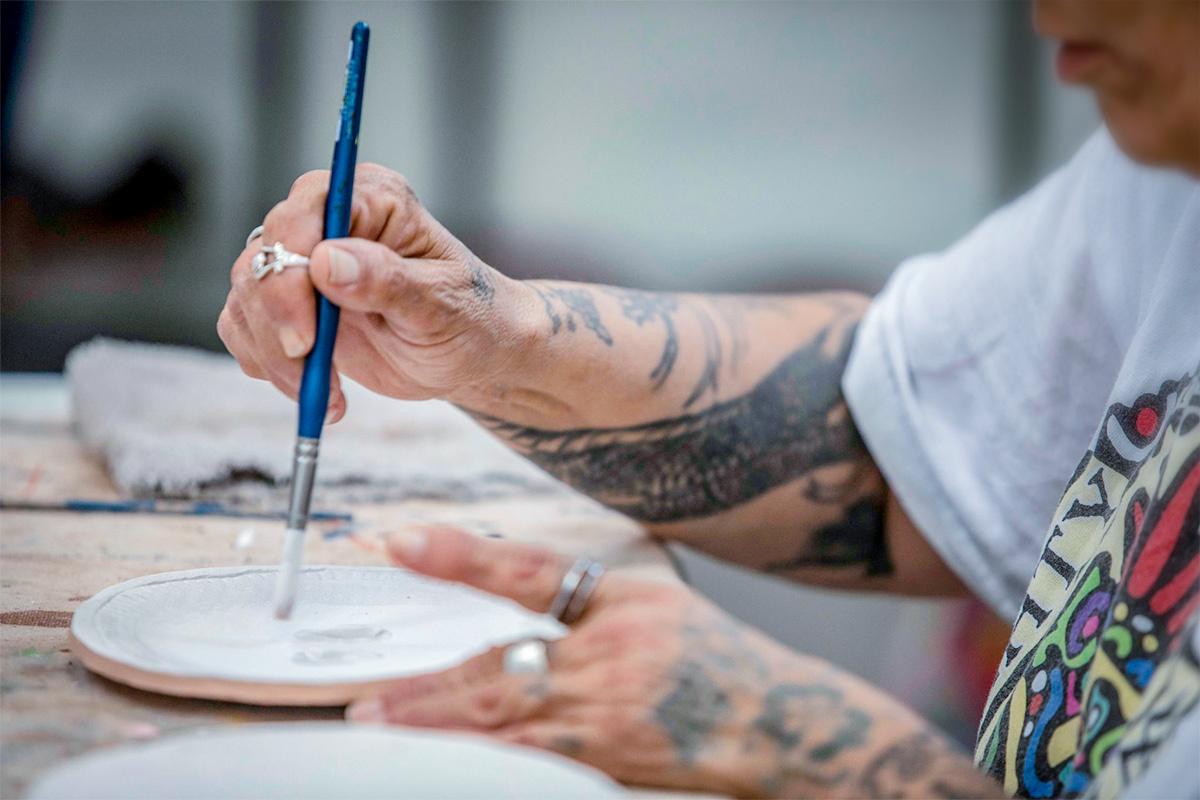 A person using a paint brush on a disk of clay.