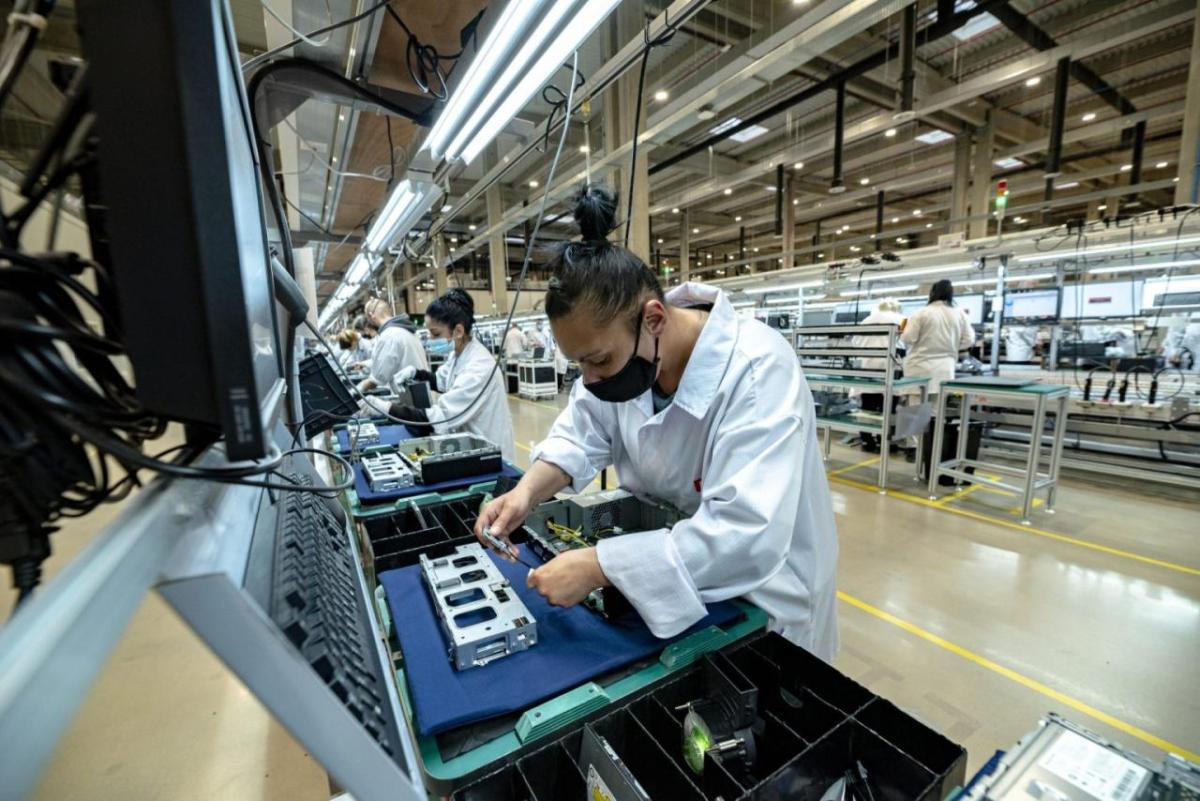 A person assembling electronics with others to the sides.