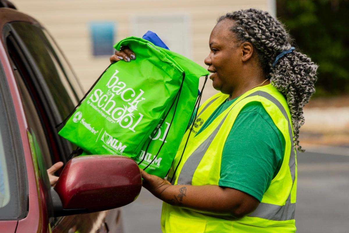 Volunteer handing bags of school supplies to community member in car