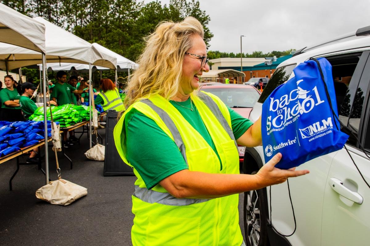 Volunteer handing backpack of school supplies to community member in car