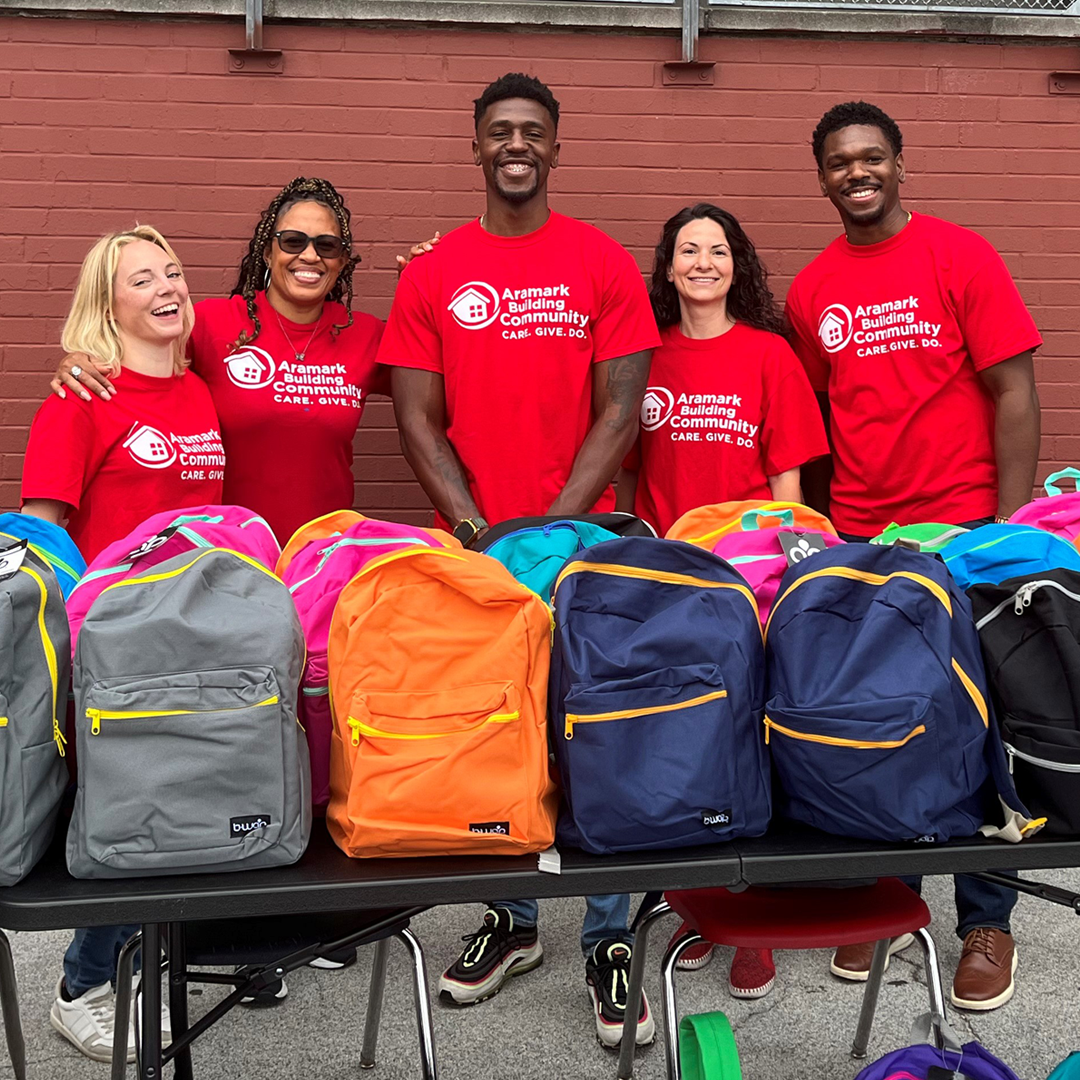 Volunteers stand behind a table of backpacks