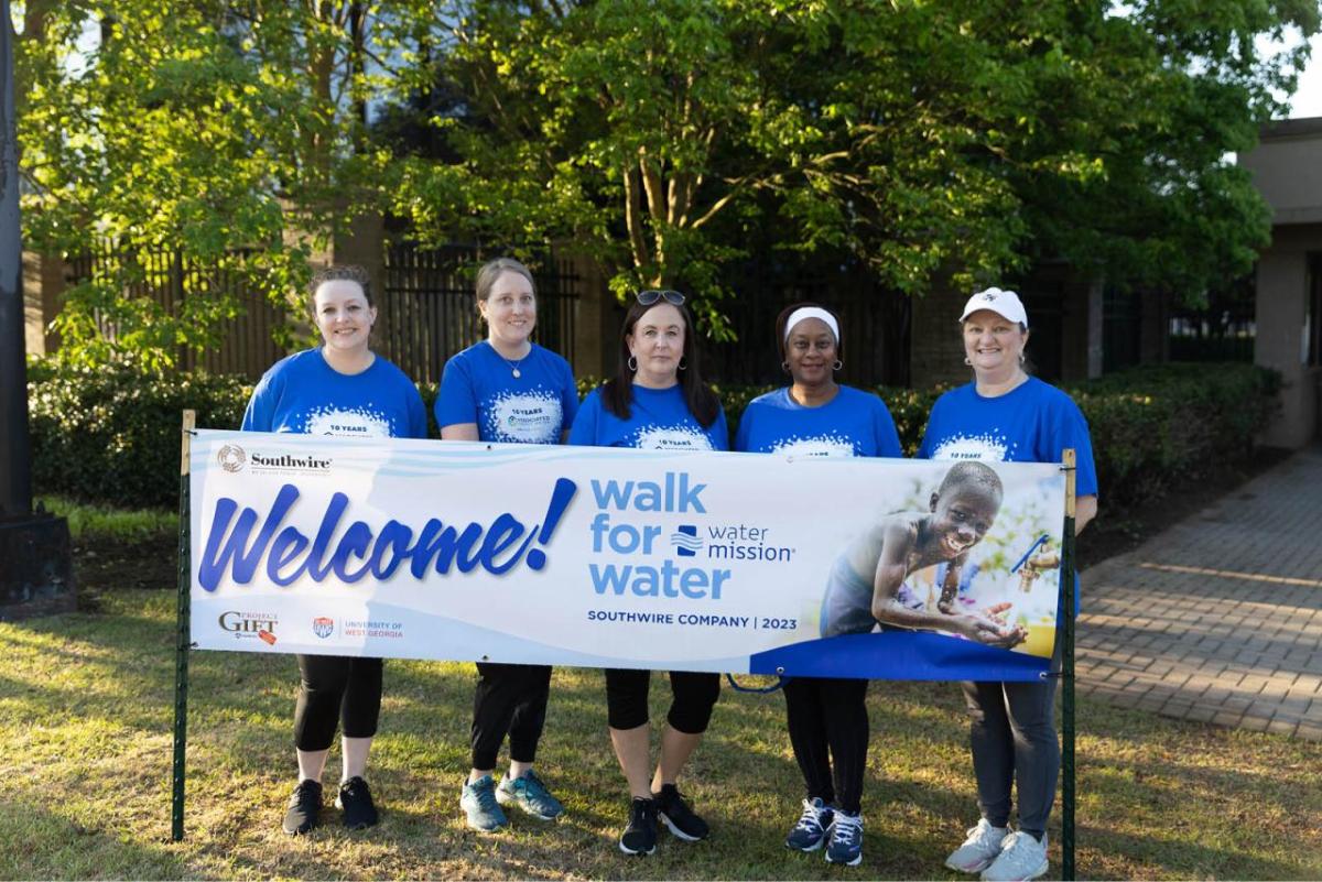 Five participants standing in front of Walk for Water banner