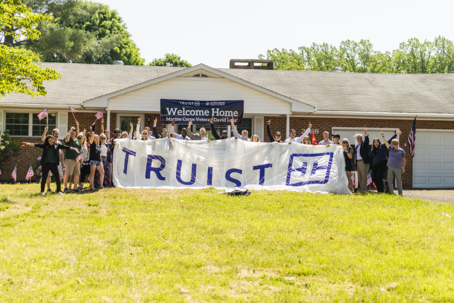 a large group of people outside the new home, a large "Truist" banner being held up