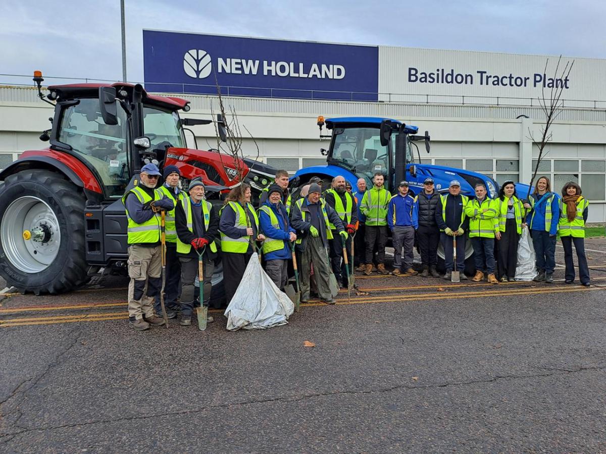 Volunteers standing together with trees to plant, in front of tractors at the Basildon Tractor Plant