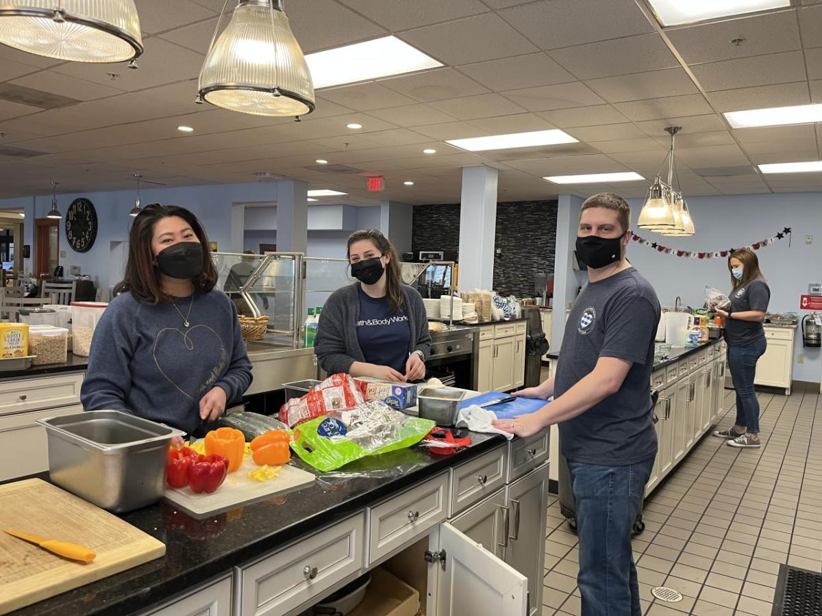 Four Bath & Body associates stand at long counter in the Ronald McDonald House preparing fresh vegetables.