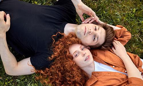 Two people lying with heads together in the grass.