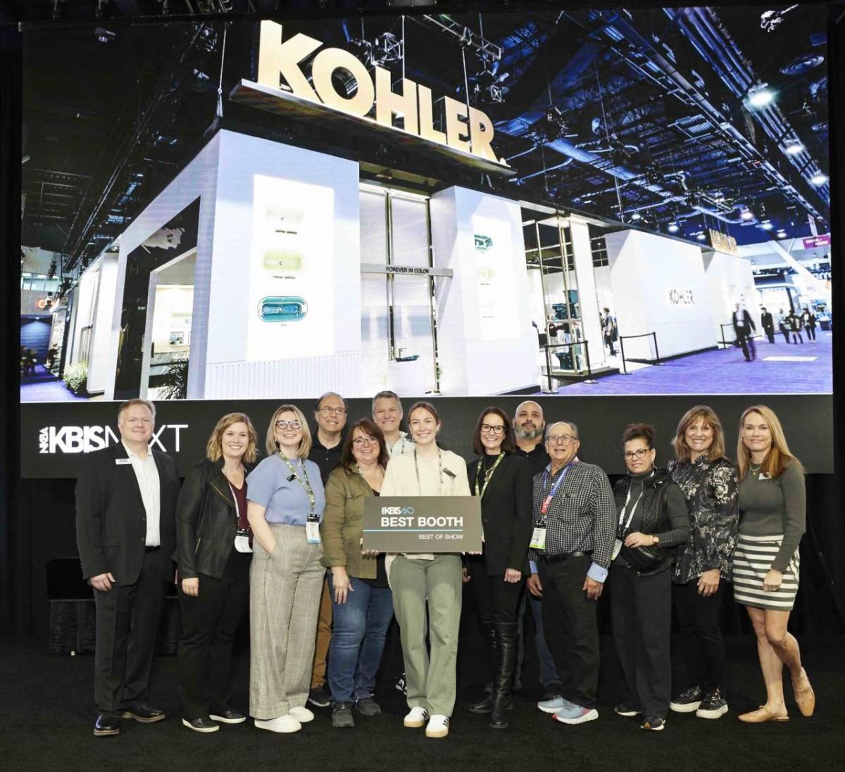 A team of people standing posed in front of the Kohler booth. One holds a sign "Best booth"