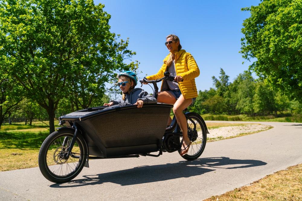 An adult operating a bicycle with large compartment in front with a child sitting inside.