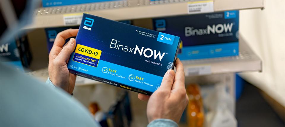 A person holding a BinaxNow Covid-19 test kit. 