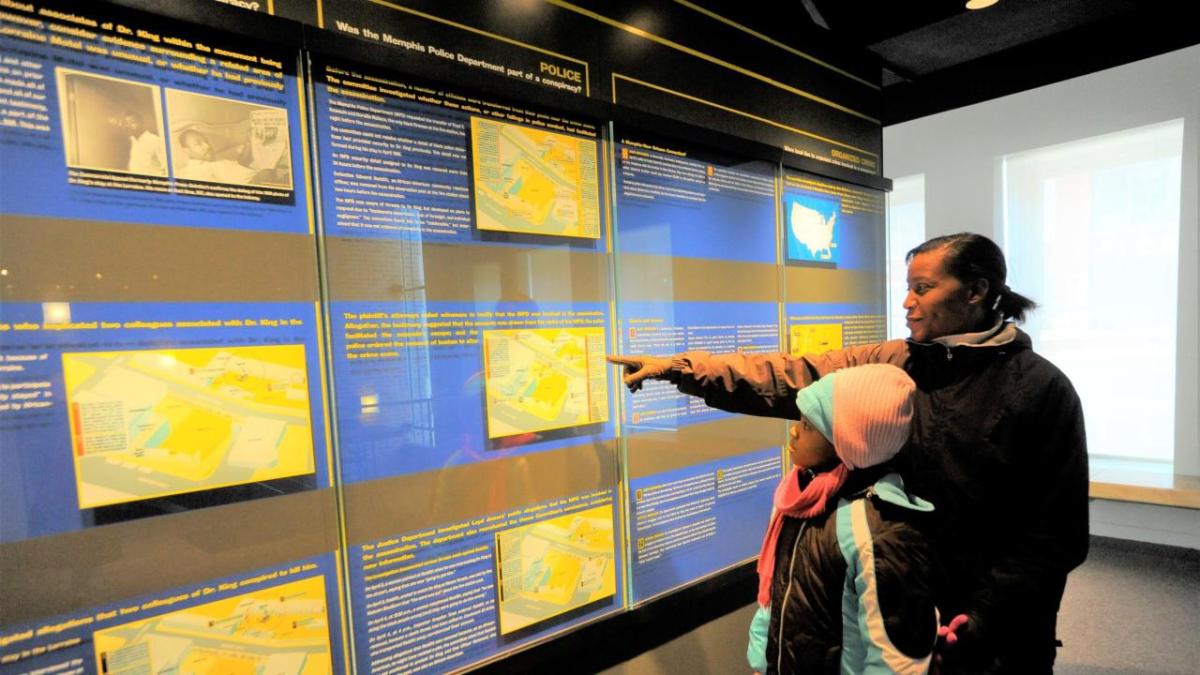 An adult pointing at a display in a museum setting. A child in front of them.