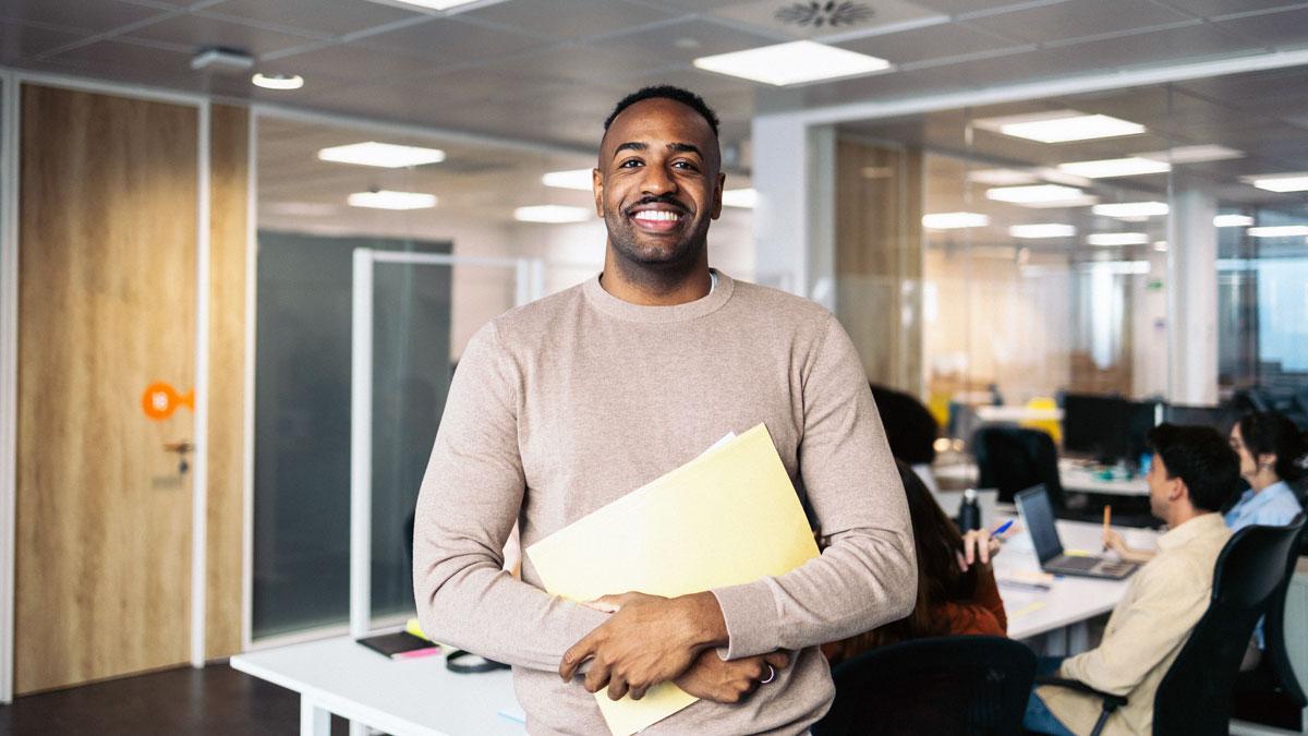 : Black adult male at work holding folder of Black History Month information