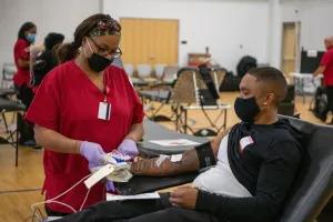 a person reclined donating blood, a healthcare worker by their side