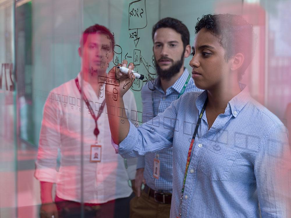 person draws on a white board while two others look on