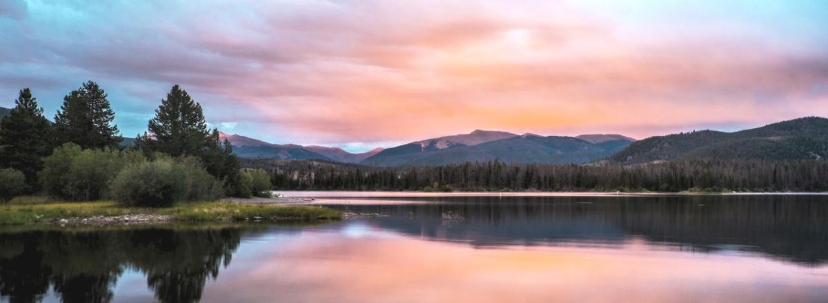 wide river and pine trees at dawn with mountains in the distance