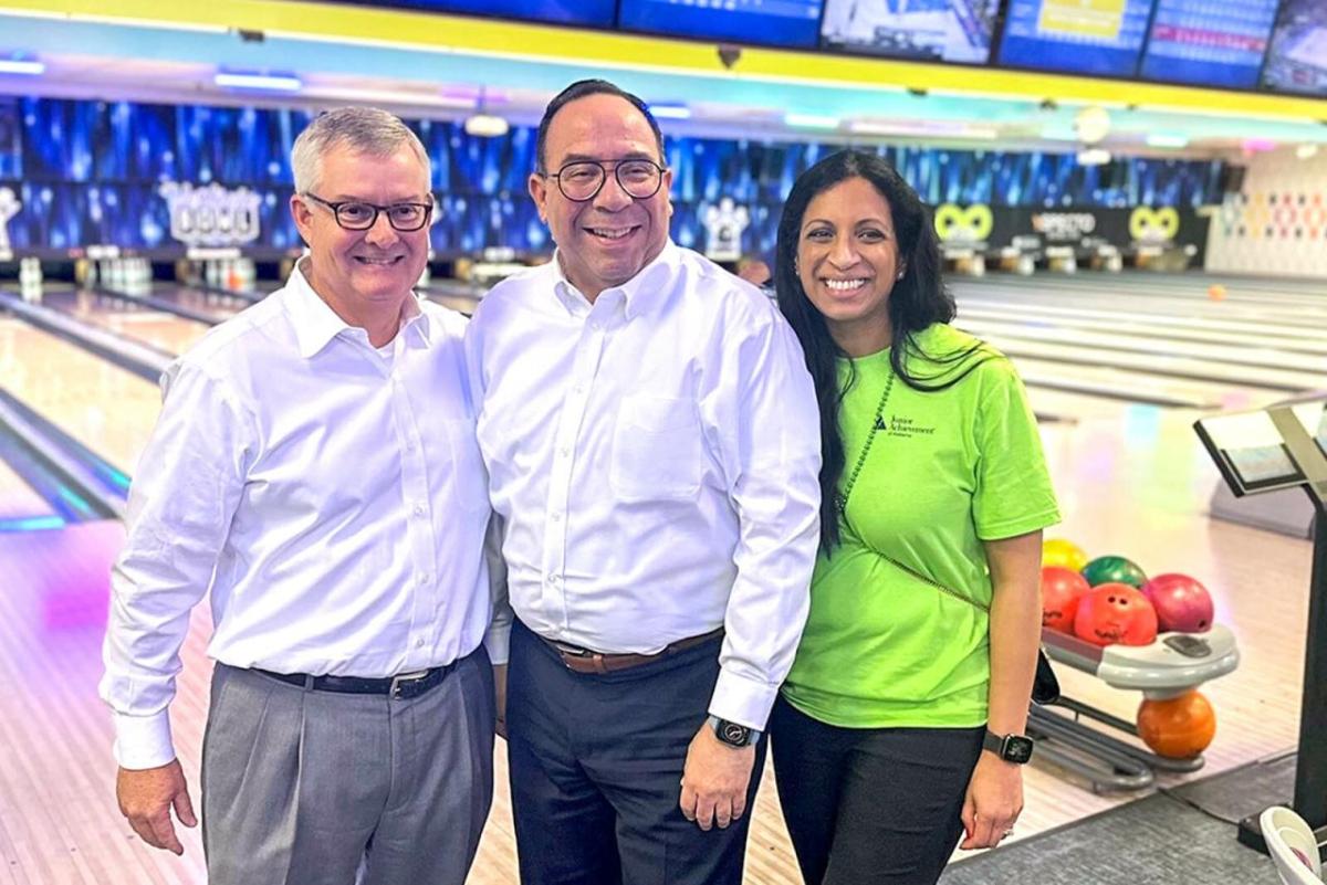 Three people posed together in a bowling alley.