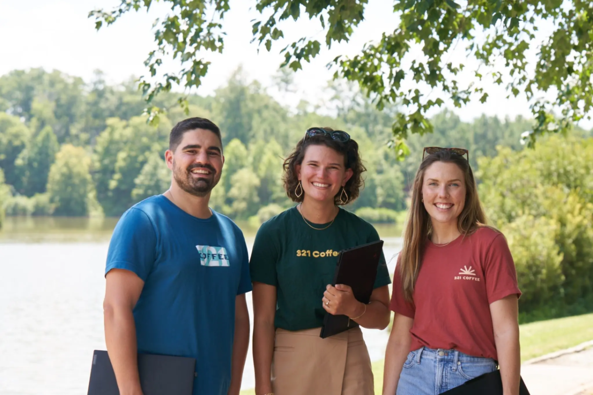 three smiling people in front of water and trees
