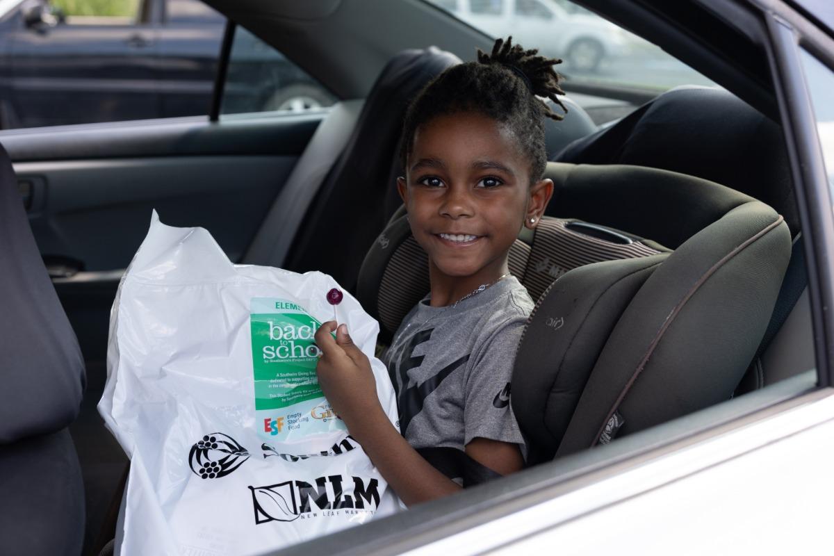 Student sitting in car holding a bag of school supplies