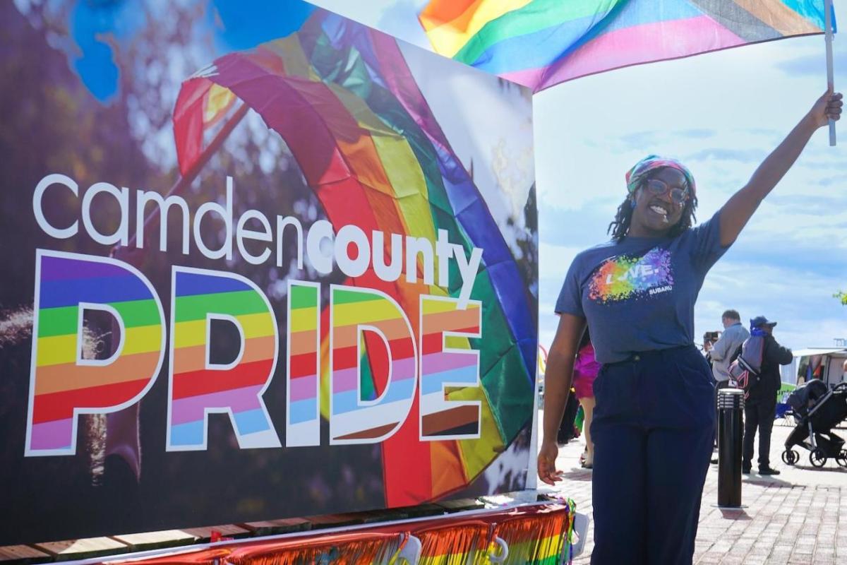 Employee resource groups such as the Out + Ally network of LGBTQ+ employees and allies help to foster inclusion and belonging at Subaru. (Image courtesy of Subaru of America) A person waving a pride flag next to a sign that says "Camden County PRIDE"