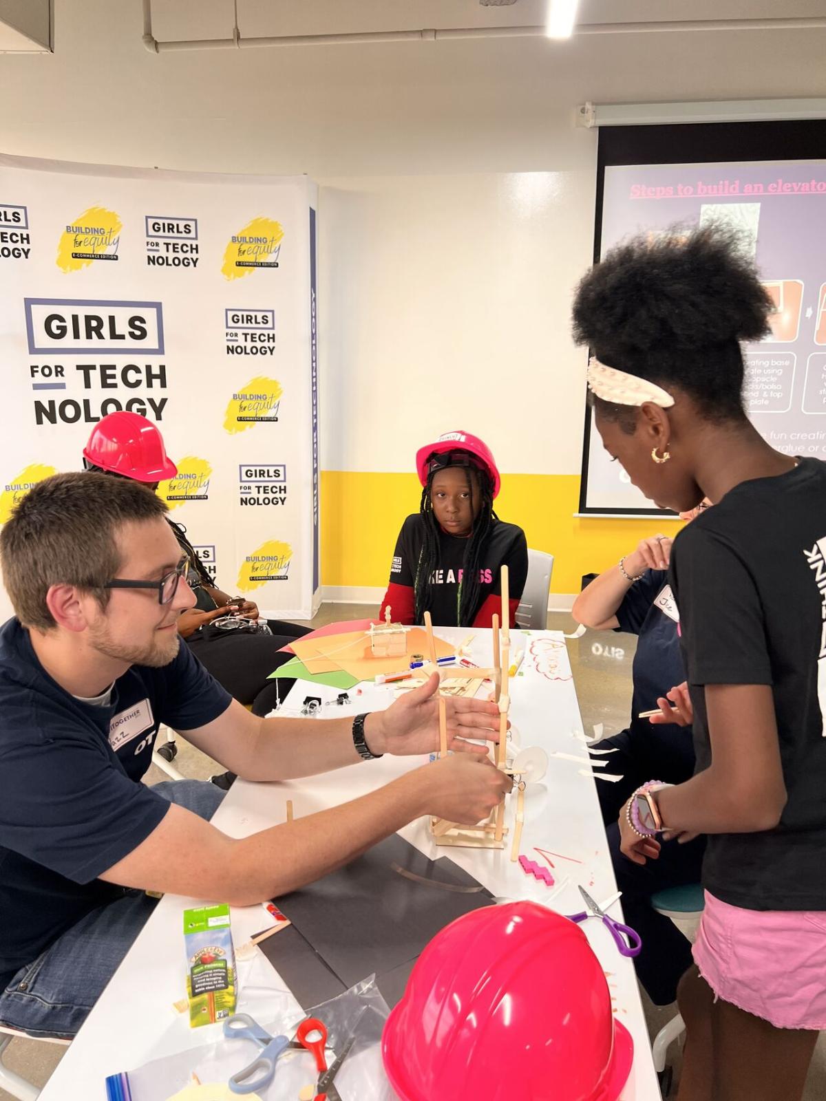 Adult volunteers and children working on building model structures with craft supplies.