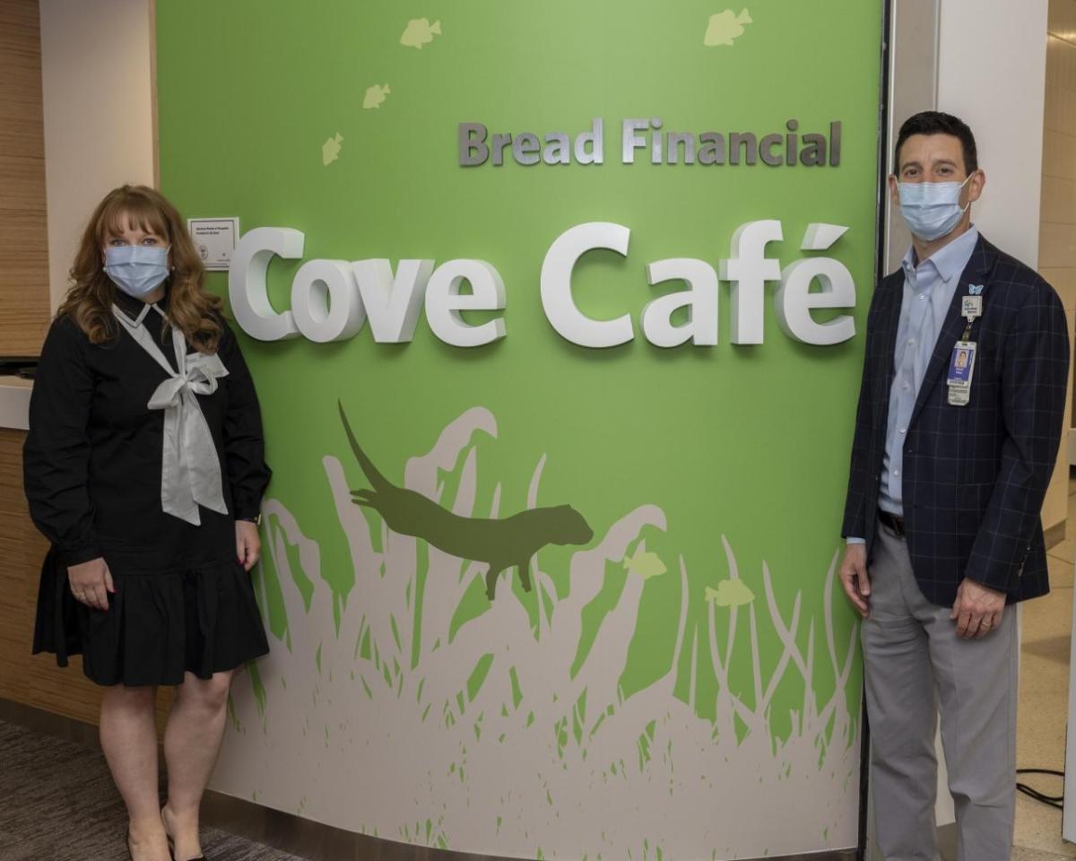 Two people in front of Bread Financial Cove Café sign