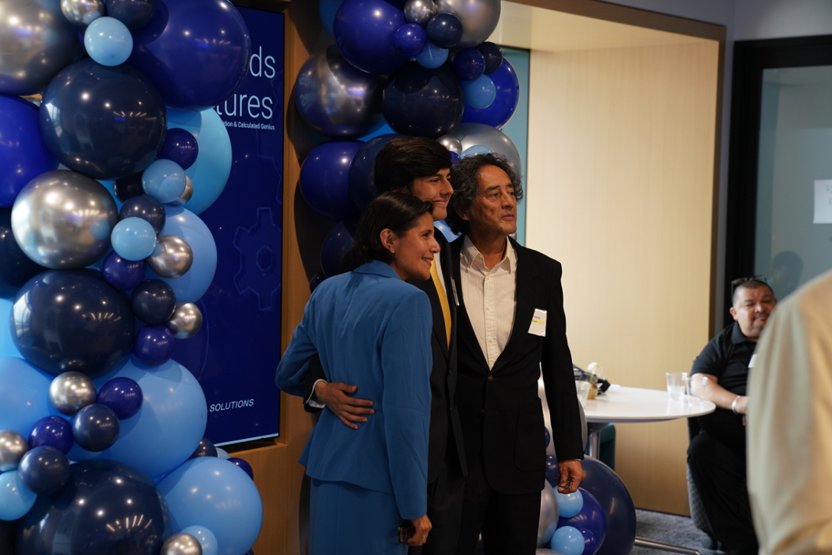 Three people posing for a camera beneath blue balloons