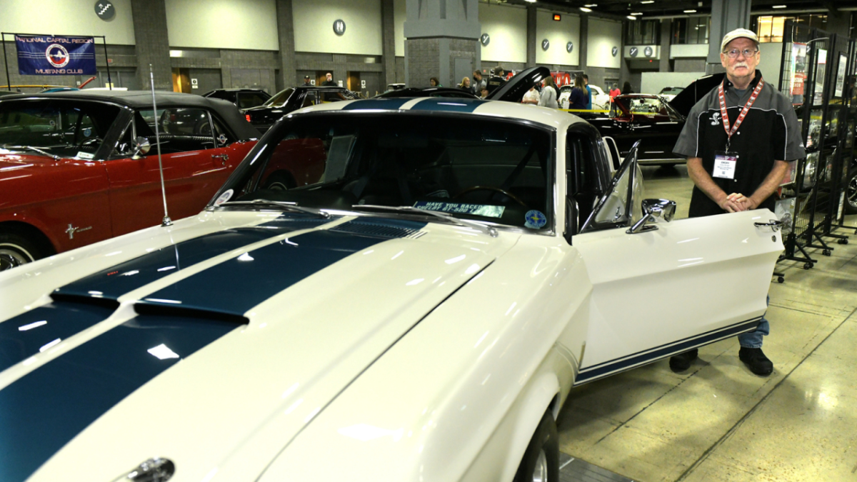 A person standing in the open door of a car at an auto show.