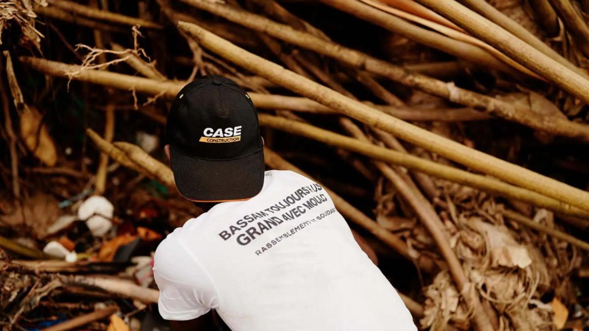 A person wearing a white t-shirt and a black cap, knelt down on the ground