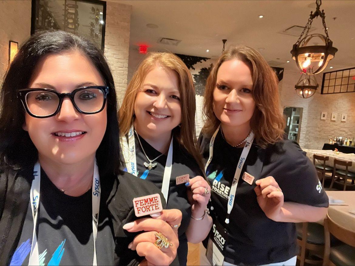Three people holding up their "Femme Forte" buttons