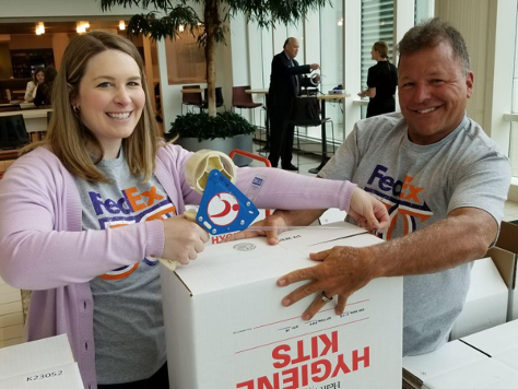 Two smiling people taping up a box that says "hygiene kits"