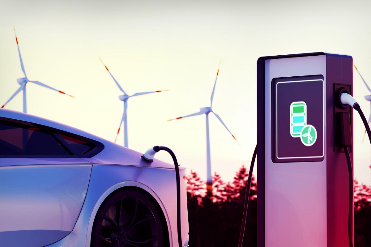 an electric vehicle plugged in to a charging station. Windmills in the background.