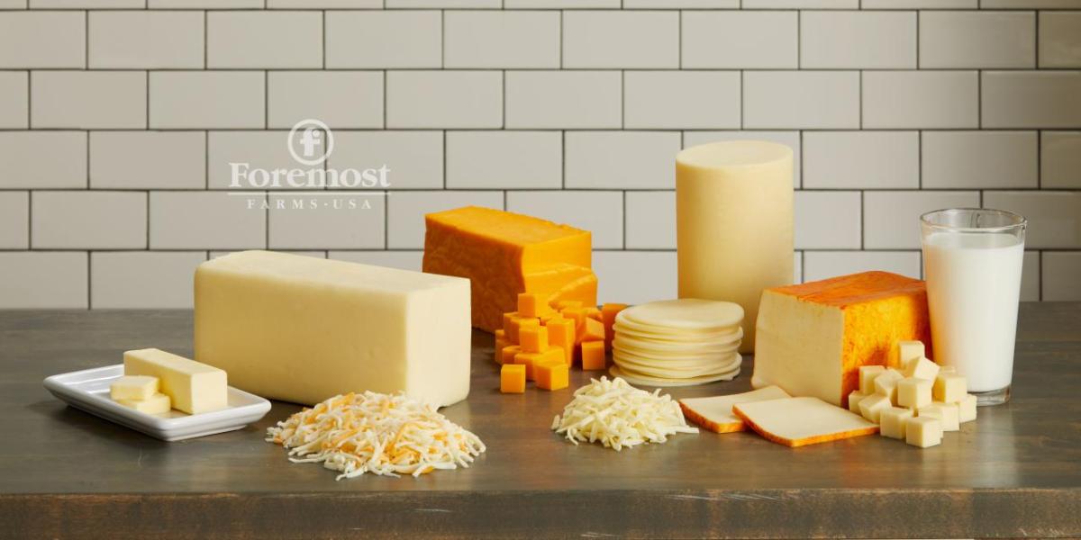 An arrangement of different cheeses and milk on a wood table.