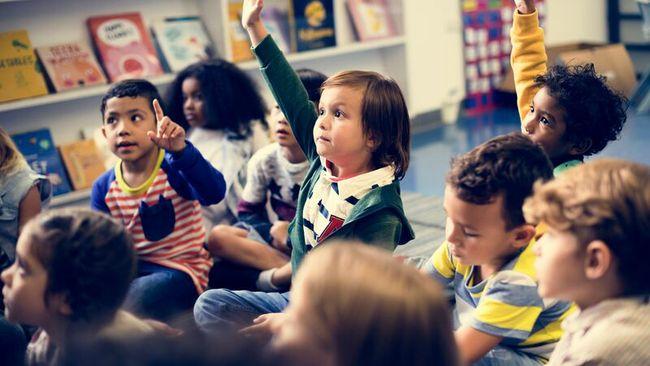 young children sitting on a classroom floor and raising their hands