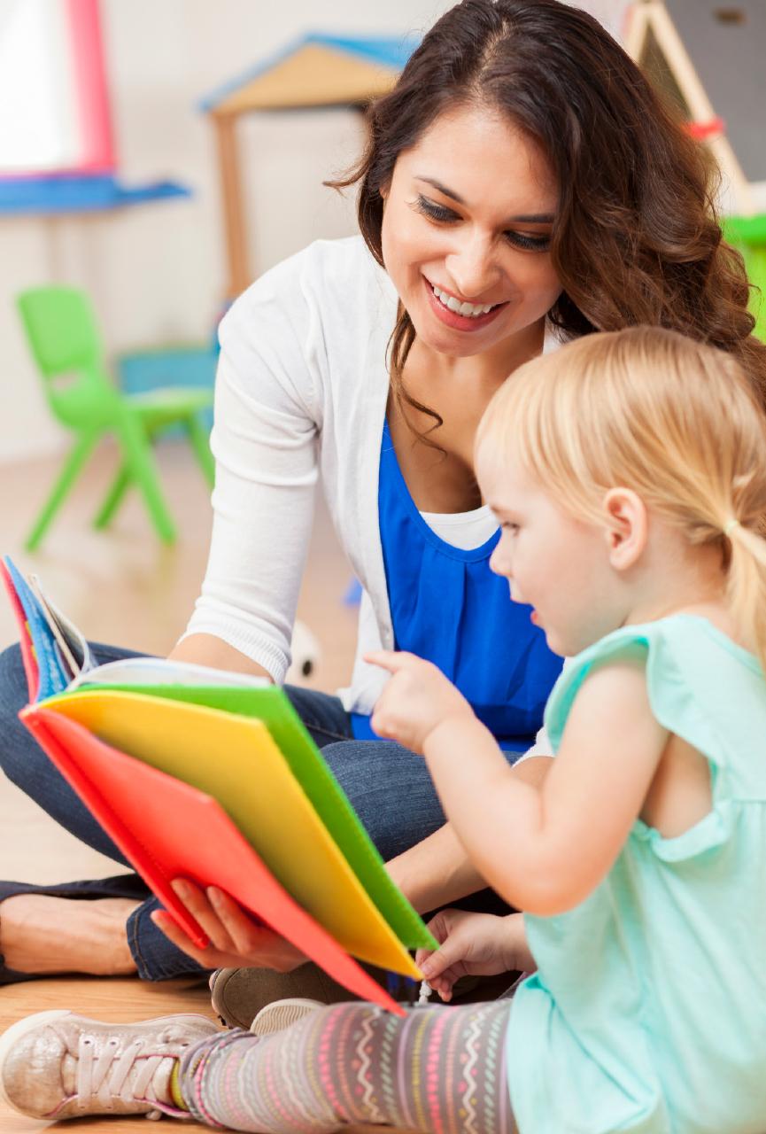 An adult reading a book with a seated child.