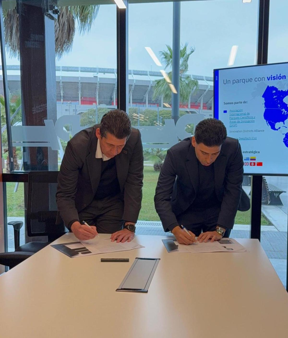 Two people signing a paper on a desk in front of a big window