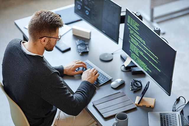 A person using a desktop computer with multiple screens.