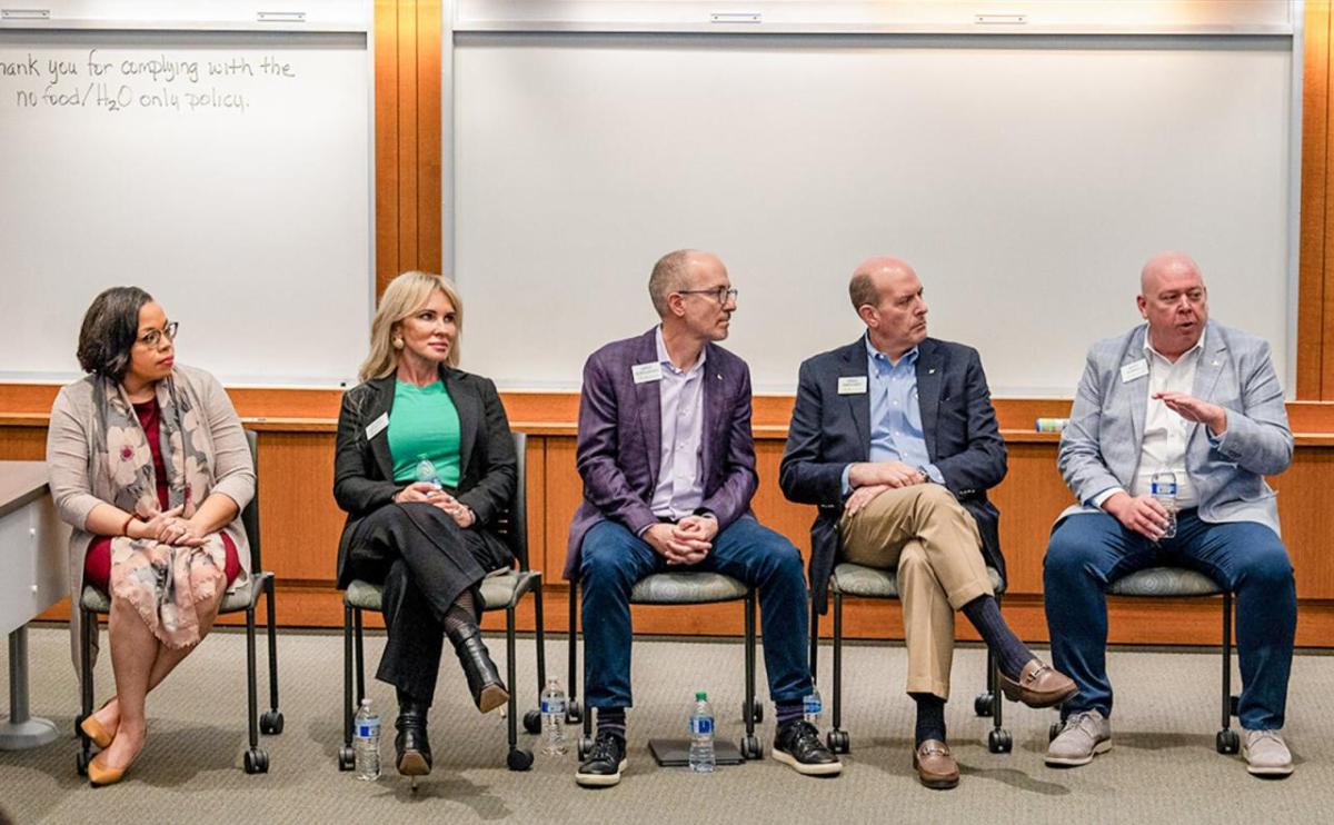 A row of seated people. One speaking. Whiteboards behind them.