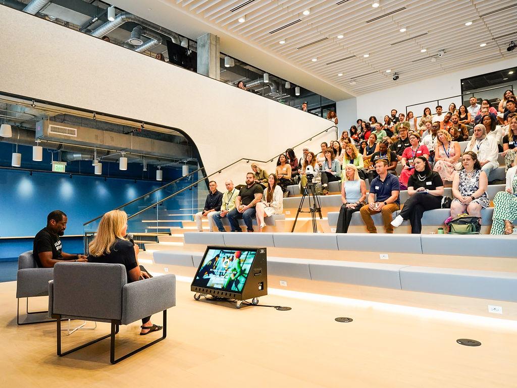 A room of seated attendees and two speakers seated in front of them.