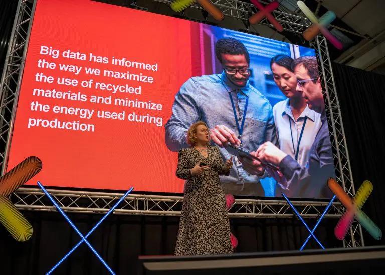 a person speaking on stage with a large projection screen behind them