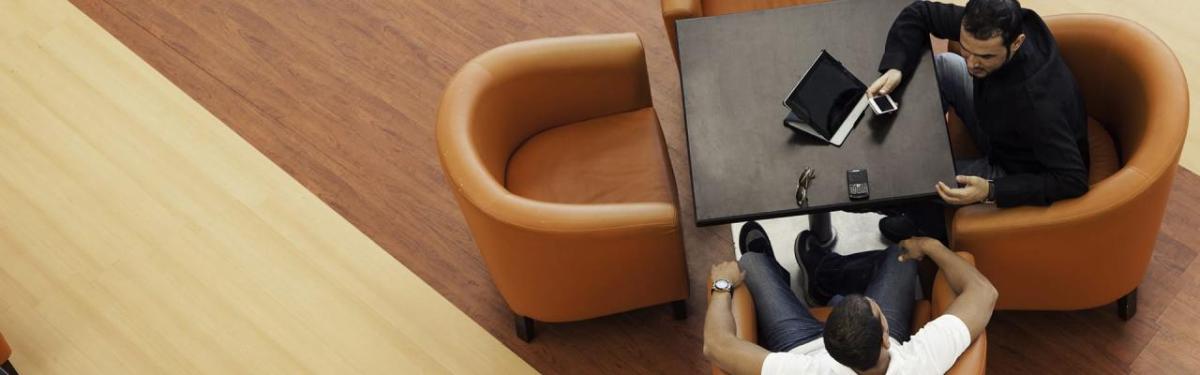 Two people seated in armchairs, a laptop open on a small table in front of them.