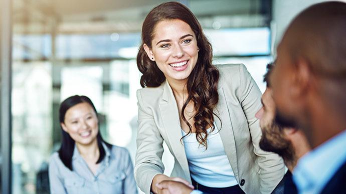 A standing person smiling at others seated in an office setting.