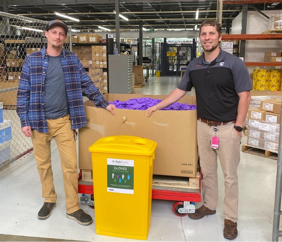 Continuous Improvement Leader, Clayton Johnson (left), and Materials Manager, Sven Creutz (right), stand next to a nitrile glove recycling container they implemented as part of the initiative. The receptacles are placed at every glove station in Columbus Mid-Range Engine Plant. " "