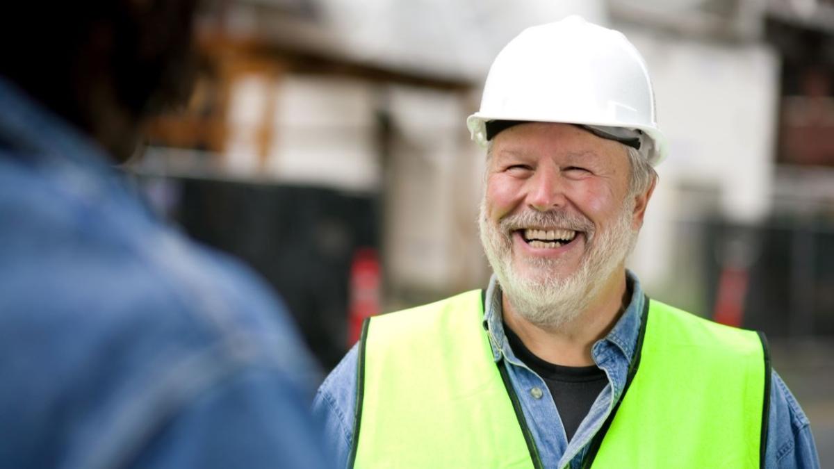 A smiling person in hard-hat and high-vis vest.