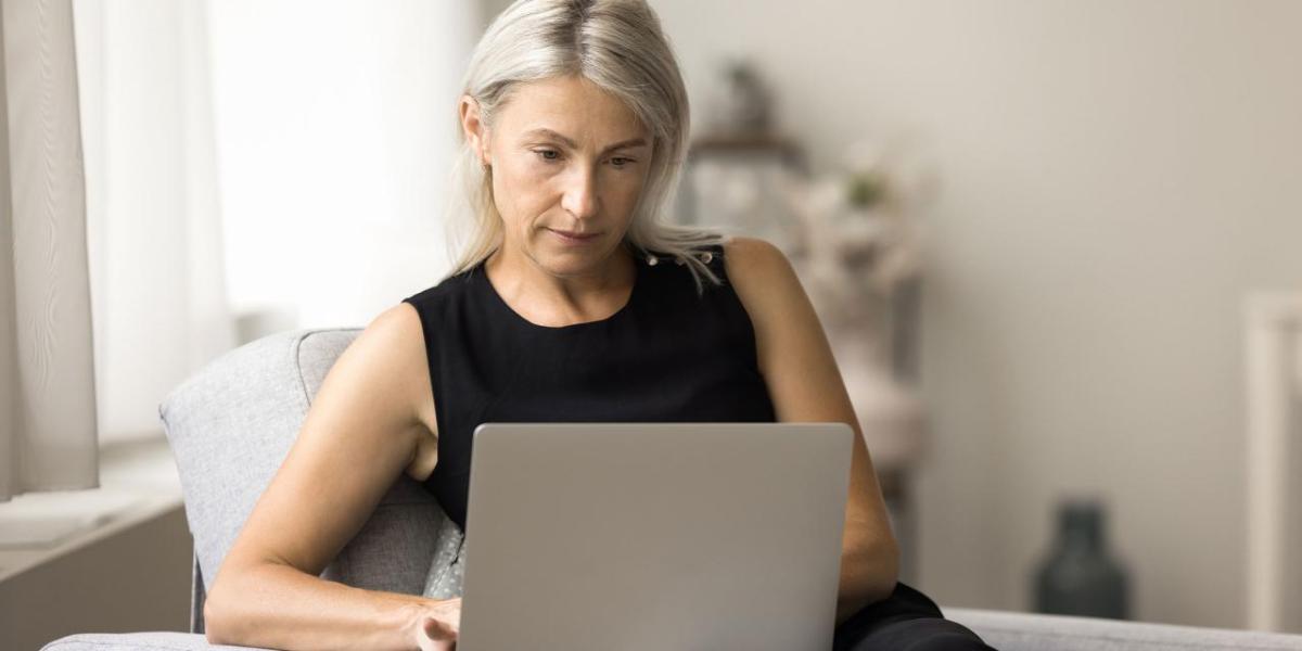 Woman seated at a table reviewing a laptop.