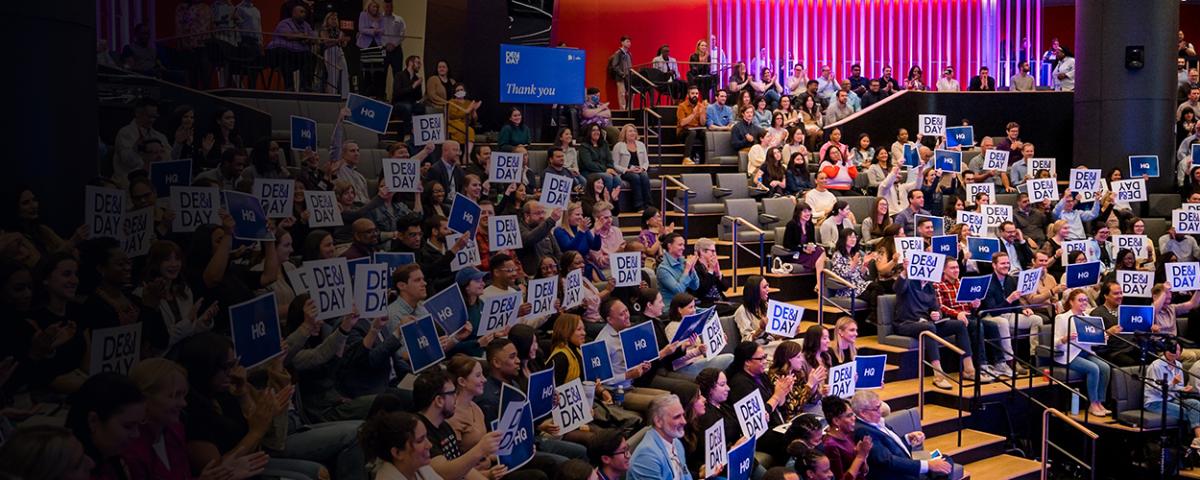 Crowd sitting in a theater at DE&I Day holding signs