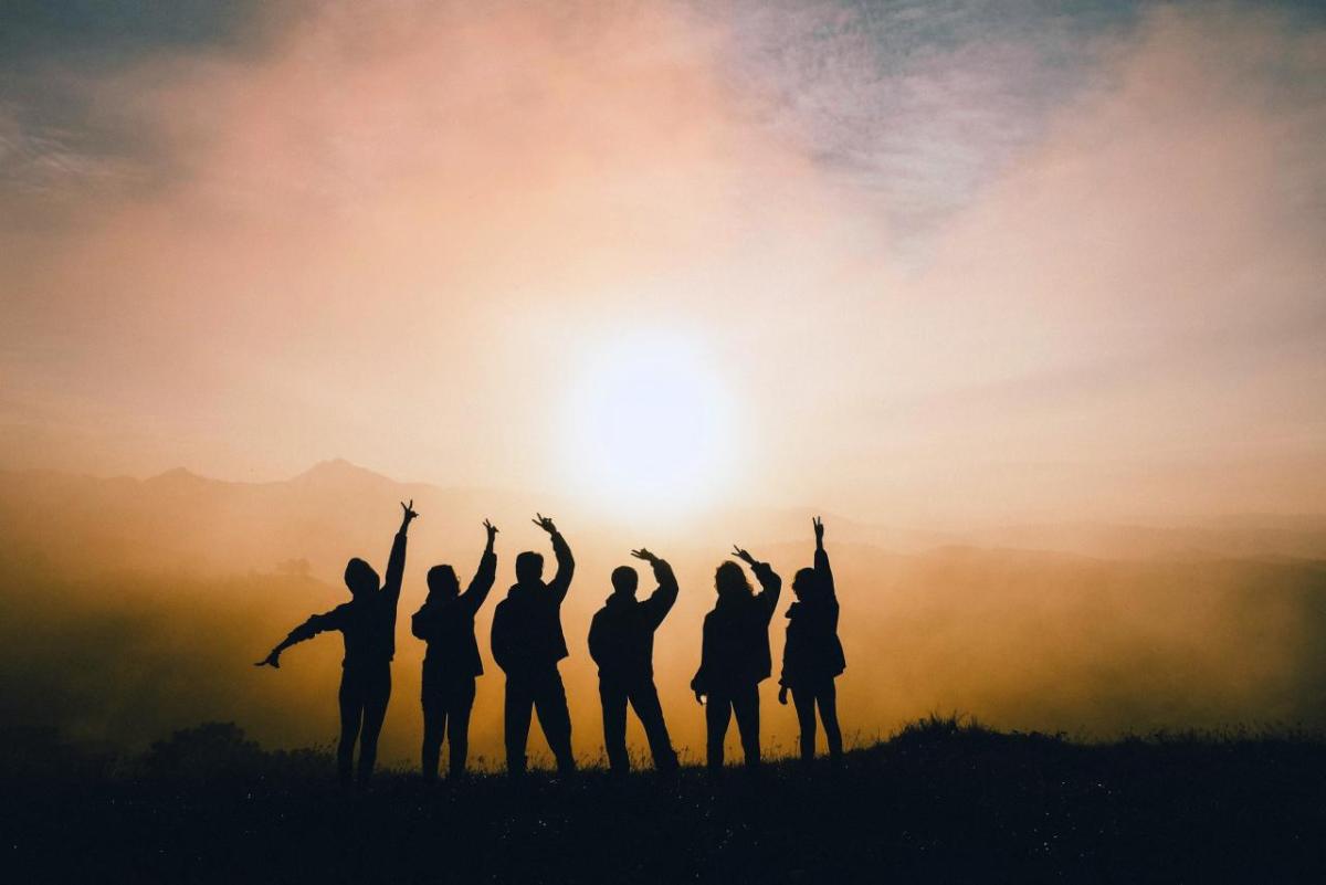 Six people in a row silhouetted against a sunset.