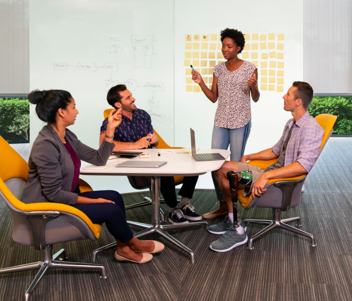 Three people seated at a conference table as a third stands, talking.