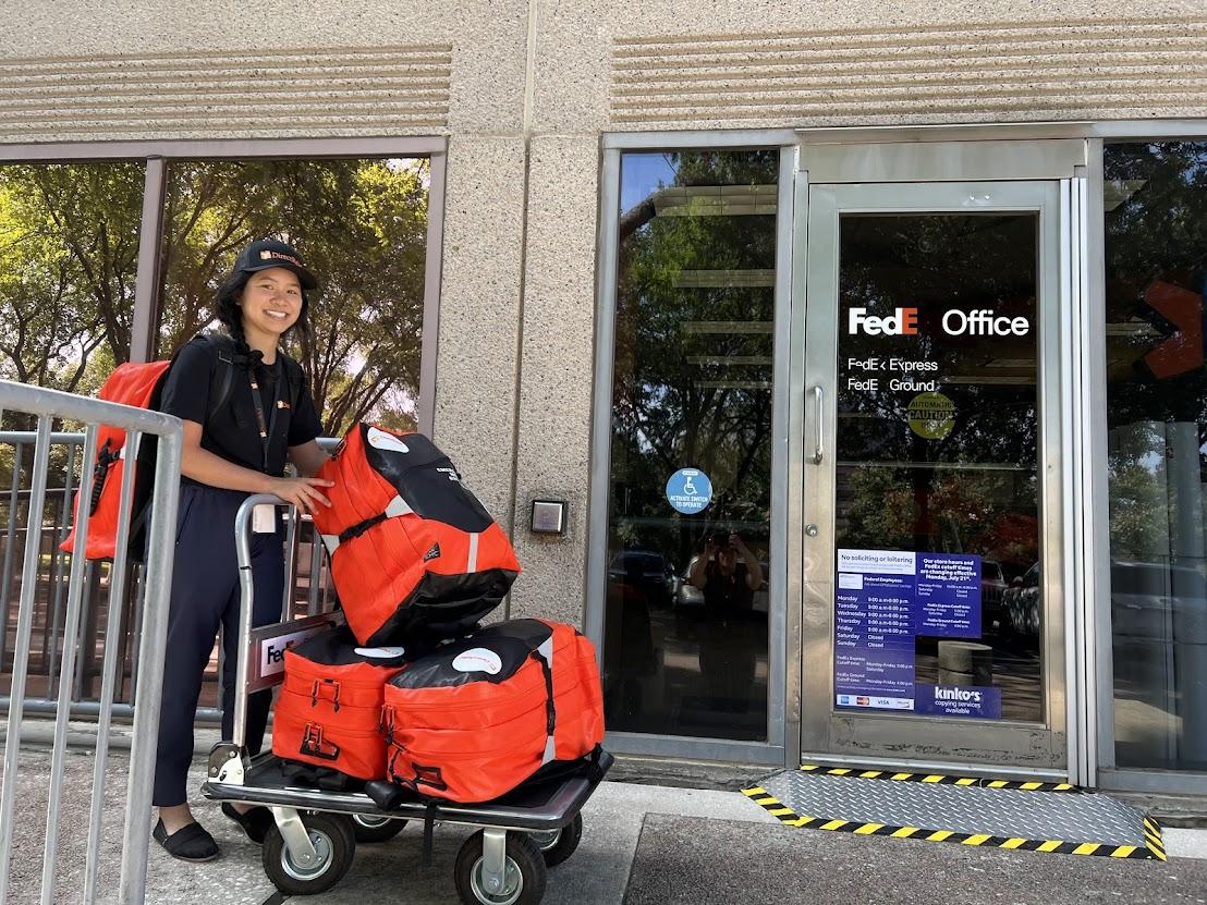 Someone rolling red bags on a trolley to a FedEx office