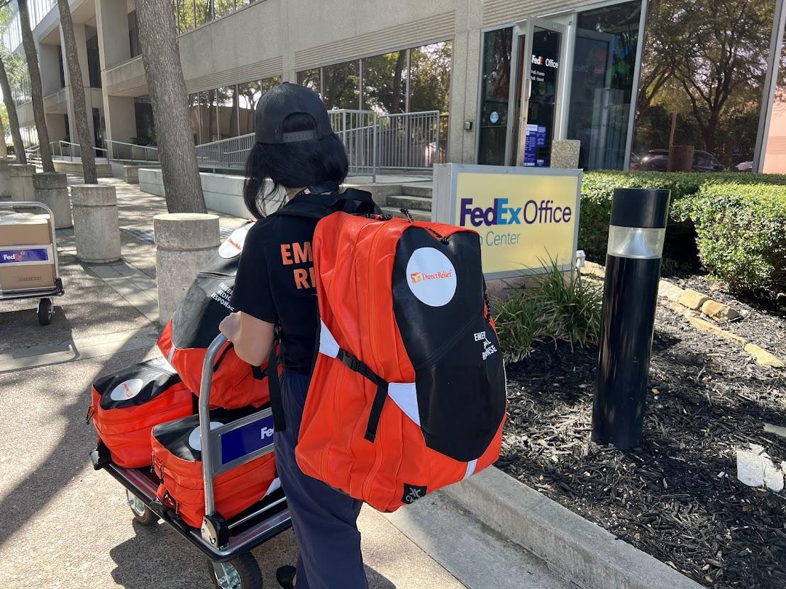 Someone rolling red bags on a trolley to a FedEx office