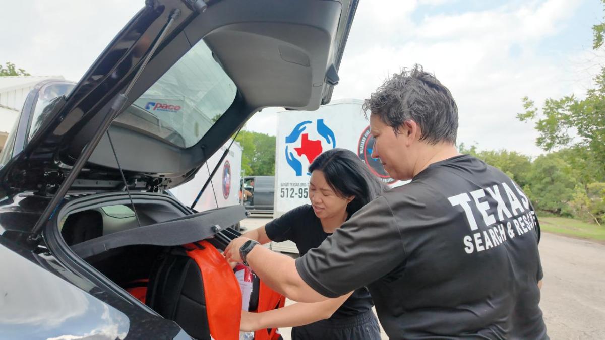 Two people putting red bags into a vehicle trunk