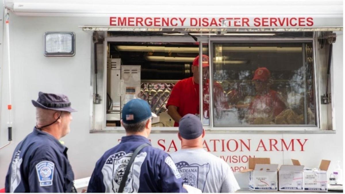 Three people in line in front of a food truck "Emergency disaster services" and Salvation army logos.
